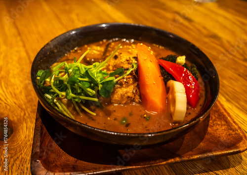Spicy curry soup, local famous popular menu in Hokkaido, with vegetables and meats, served in black bowl on wooden table in restaurant in Japan