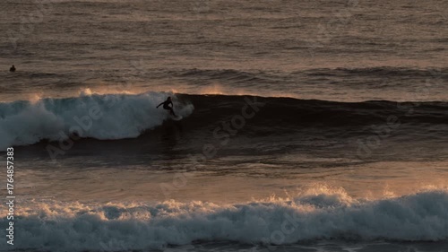 Male surfer skillfully navigates a large wave as the sun sets