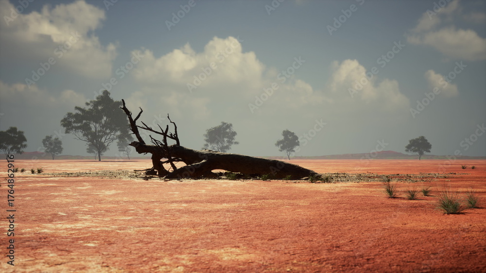 Fototapeta premium Barren terrain stretches under a vast sky, featuring a prominent fallen tree with dry branches. Sparse vegetation dots the ground, creating a haunting yet beautiful scene of natures resilience.
