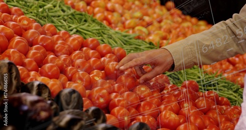 Touching tomato with shopper's hand in produce section, with red tomatoes green beans and eggplants