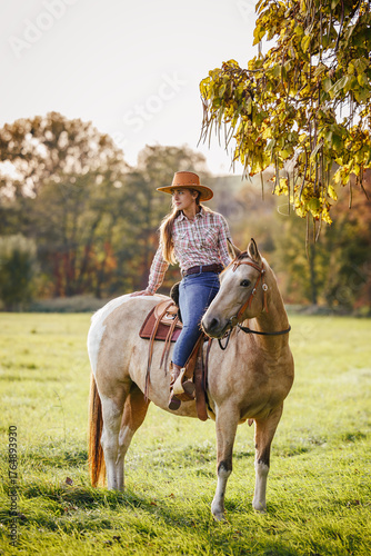 Woman rider resting on horse at autumn rural scenery. Cowgirl horseback riding in western style