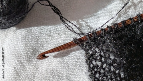 Wooden Crochet Hook with Black Yarn. Close-up of a wooden Tunisian and knooking crochet hook working with black yarn, next to a ball of matching thread on white linen background.