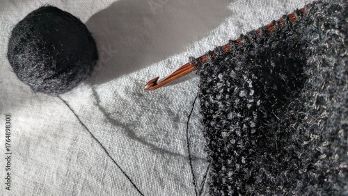 Wooden Crochet Hook with Black Yarn. Close-up of a wooden Tunisian and knooking crochet hook working with black yarn, next to a ball of matching thread on white linen background.