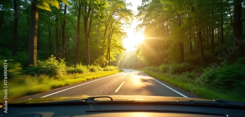 View from car driving along road through green forest. Bright sunlight shines down creating warm atmosphere. Road trip adventure in nature. Scenic drive through trees on summer day.