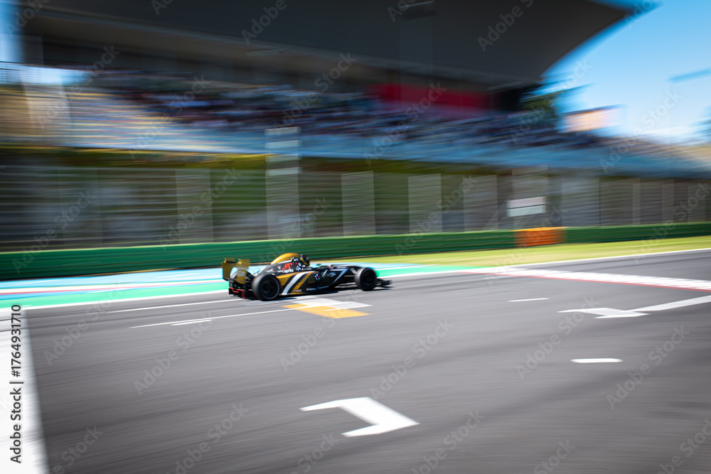 Fototapeta premium Blurred motion image of formula racing car on asphalt circuit main straight with grandstand in background