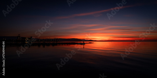 Vibrant sunset over the ocean with city lights.