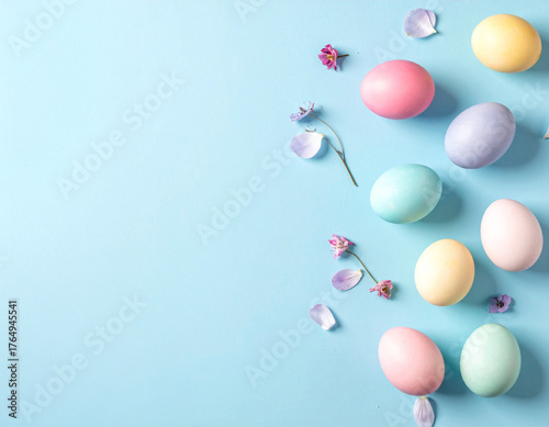 Minimalist Easter flat lay with smooth, solid pastel eggs and scattered delicate flower petals on a bright blue background with extensive copy space.