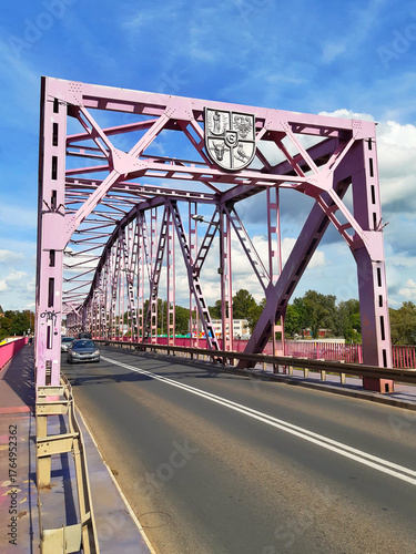 Vibrant pink Tolerance bridge spans muddy river under cloudy sky
