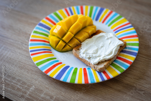 Deliciously vibrant mango slices and creamy spread on toast presented on a colorful striped plate, offering a delightful breakfast or snack.