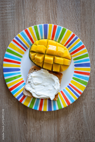 Delightful breakfast featuring a fresh mango half and creamy toast on a vibrant, colorful plate against a rustic wooden background, perfect for healthy eating concepts.