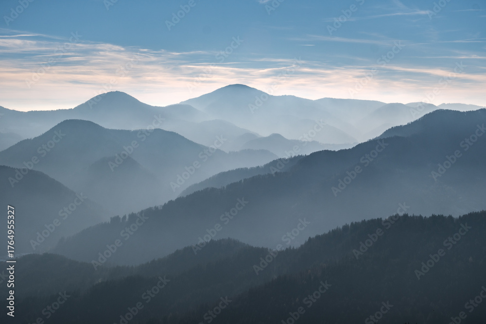 Obraz premium Misty mountain layers under a soft blue sky.