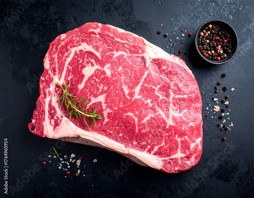 Top view of a raw, dry-aged Wagyu cutlet steak with high marbling, seasoned with rosemary, salt, and pepper on a dark black background.