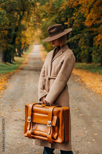 European woman in coat and hat walks along  yellow autumn trees
