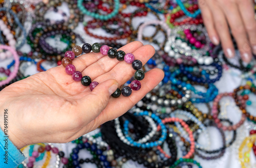 Hand holding colorful gemstone bracelet made of natural stone beads, handmade jewelry displayed at craft market or gemstone fair