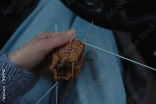 	
knitting sweater in glove in brown color on four circular needles while sitting in a car	
