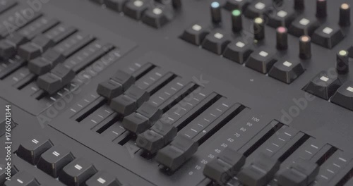 Sound engineer's console, level controls move up and down. Close-up handheld shot, real time speed, artificial indoors lighting.