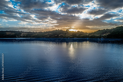 Dramatic sunset over a tranquil lake with rolling hills and cloudy skies