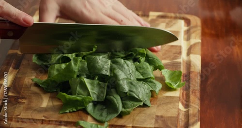 Close up of person cutting fresh spinach on wooden board, preparing ingredients for healthy vegan meal, organic cooking process, green vegetables, rustic kitchen atmosphere, natural lifestyle.