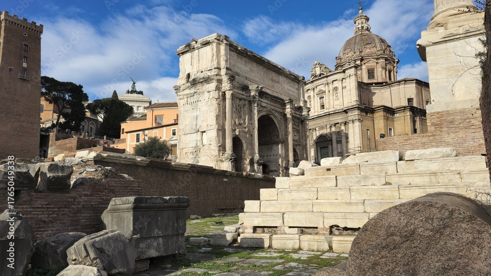 Obraz premium Rome, Italy – 13 January 2025. The Arch of Septimius Severus rises among Roman Forum ruins with Santi Luca e Martina’s dome under a bright winter sky.