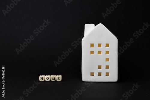 White ceramic house figurine with cut-out windows beside wooden blocks spelling home, representing finance and technology in modern living. copy space