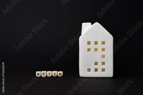 White ceramic house model stands beside wooden blocks spelling 'BUILD', representing construction, architecture, and real estate concepts in finance. copy space