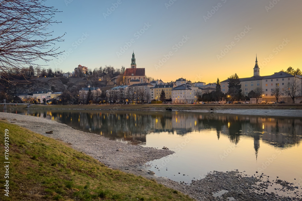 Fototapeta premium Cityscape of Salzburg, Austria at sunset with the church Maria Himmelfahrt and the Mönchsberg hill reflected in the Salzach river