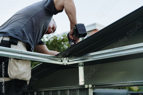 Mature worker installing roofing sheets with drill on metal shed.