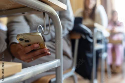 Student using smartphone discreetly in classroom under desk