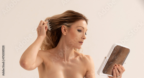 Salisbury Wiltshire England UK. 17.08.2023.  Topless woman using  a mirror and  a comb to style her hair. Studio shoot.