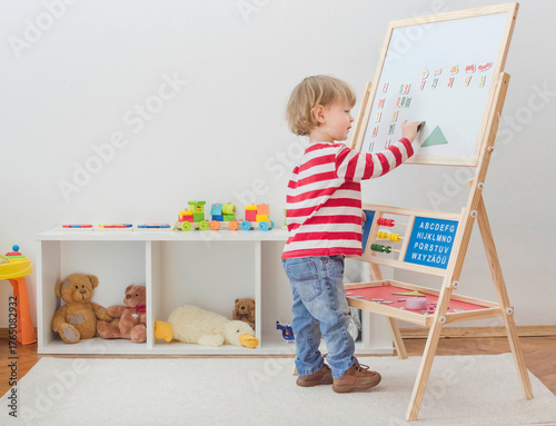 Cute little child playing at a magnetic board, learning letters, numbers and geometric shapes at home. Educative and funny indoor activity for early development.