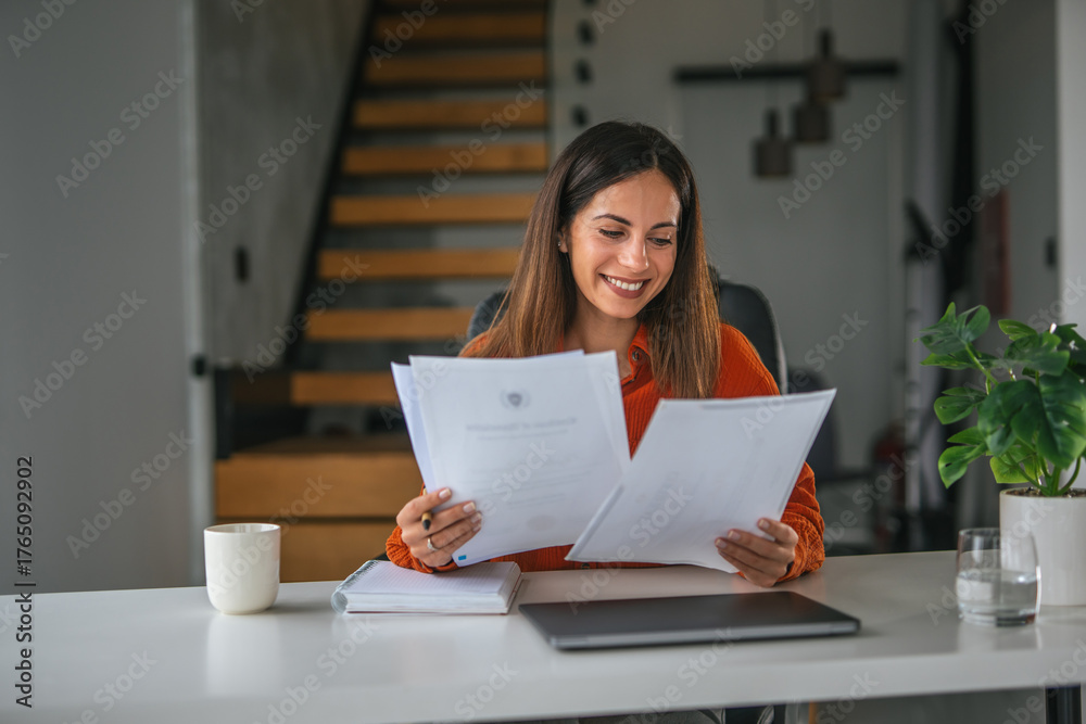 Fototapeta premium Woman reading documents smiling working from home office