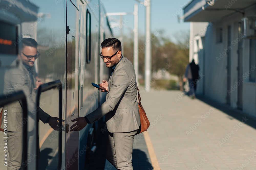Obraz premium Businessman boarding train while using smartphone at station platform