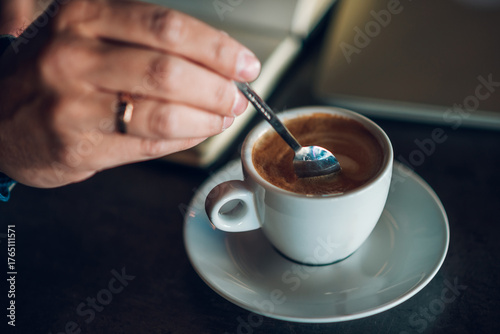 Photos Close up of man stirring coffee in cafe with book and laptop