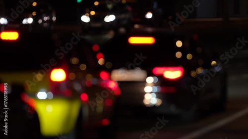Out-of-focus nighttime traffic scene with blurred car lights and brake lights glowing on an urban street. Bokeh effect, city transportation, evening commute, moody urban atmosphere