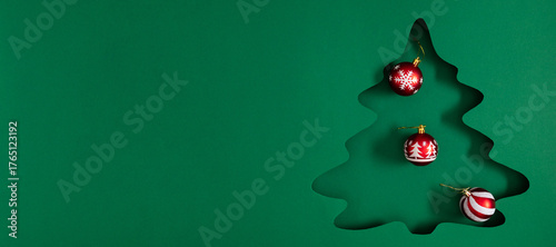 Minimalist Christmas composition with tree cutout and red ornaments on green background. Modern festive design for holiday cards, banners, and winter greetings.
