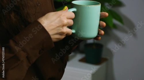 Closeup hands video of business woman holding in hands mug with coffee and relax drinking in office, room interior with green flower. Business concept	
