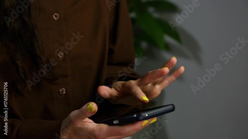 Closeup hands video of business woman holding in hands mobile phone and working, texting, chatting in office, room interior with green flower. Concept	
