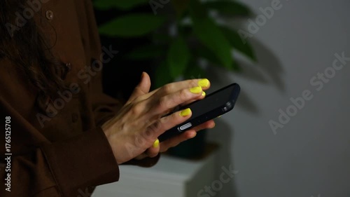 Closeup hands video of business woman holding in hands mobile phone and working, texting, chatting in office, room interior with green flower. Concept	

