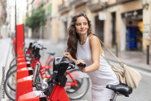 Photography Young woman in summer dress on rented electric bike on city street