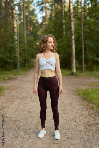 A Fit and Active Woman Standing Vibrantly on a Scenic Forest Path Surrounded by Nature
