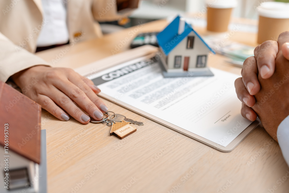 Fototapeta premium A real estate agent presents a property sale contract to a client, discussing agreement details with a model house on the document, symbolizing home buying, selling, and real estate investment.