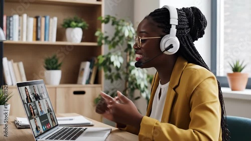 Online Meeting at Home - A businesswoman wearing headphones is using her computer to attend an online group video conference meeting while working from home.
