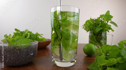 Straw stirring glass of water with mint leaves and lemon slices on wooden table.