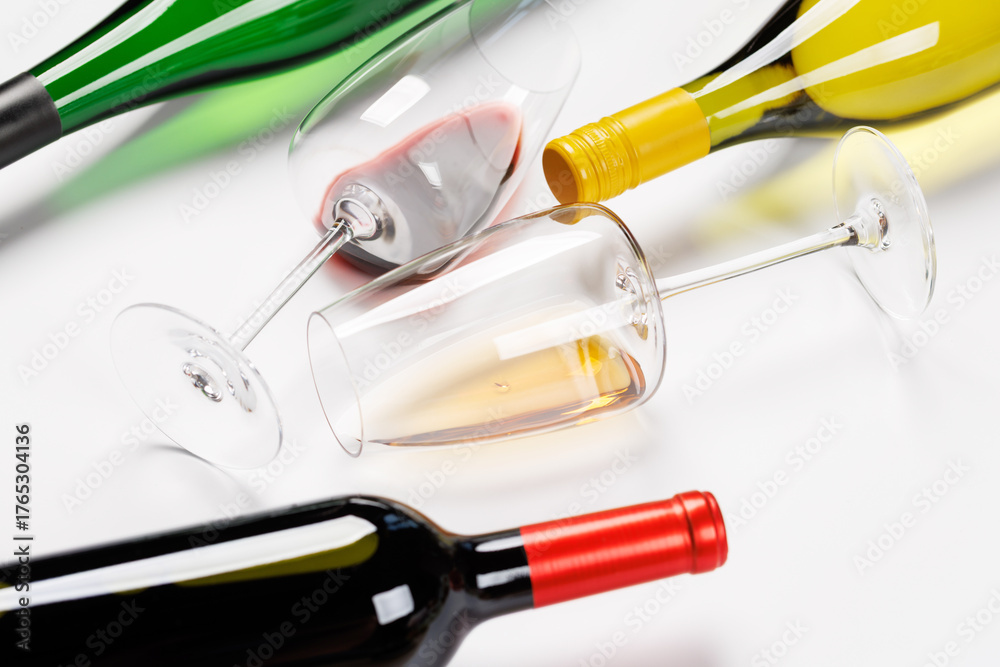 Naklejka premium Wine glasses with red and white wine and bottles lying on white background