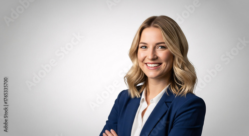 Young smiling businesswoman in a dark blue suit, looking confidently at the camera with her arms crossed, isolated on a light grey background