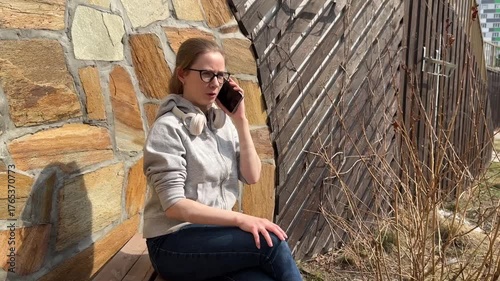 A young woman is talking on the phone while sitting on a bench. 