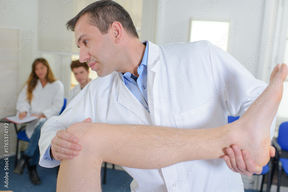 Fototapeta premium Doctor bending patient's leg, students watching