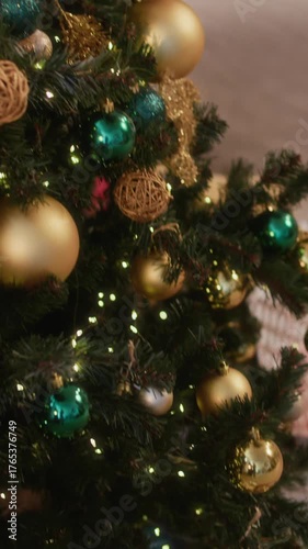Vertical of beautifully decorated Christmas tree with glowing lights, golden and green ornaments, and neatly wrapped gifts tied with ribbons placed on cozy carpet beneath