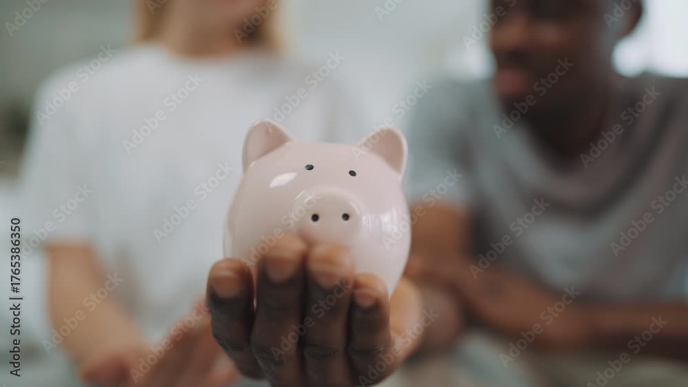 Closeup of funny ceramic piggy bank in hand of black man, woman putting ...