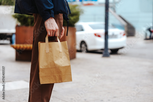 Individual holding a brown paper bag while standing on a city street in daytime